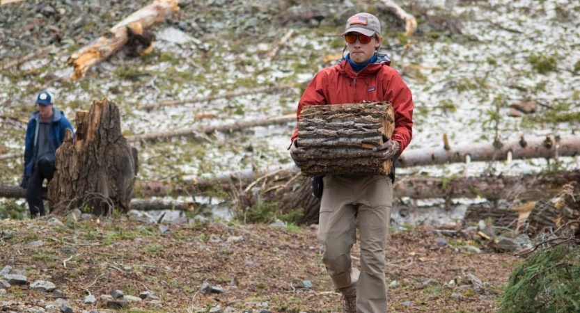 a person carries a stump during a service project with outward bound